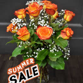 Orange and yellow roses in a glass vase with white filler flowers