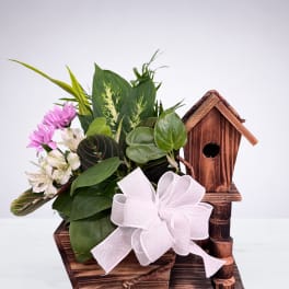 Lush green plants with pink and white flowers in a rustic wooden birdhouse planter with a white bow