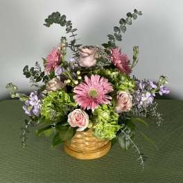 Pink gerbera daisies and roses in a woven basket with lavender accents
