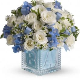 White roses and blue flowers in a clear glass cube vase