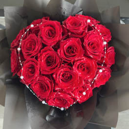 Heart-shaped bouquet of red roses wrapped in black paper with pearl accents