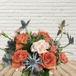 Orange and blush roses with blue thistle in a low bouquet