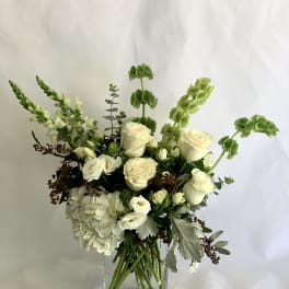 White floral arrangement in a clear square vase with tall green accents