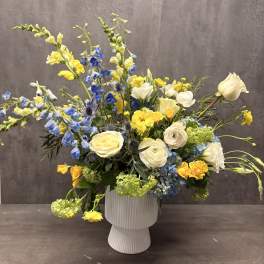 Blue and yellow mixed flower arrangement in a white vase