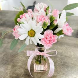 Pink carnations and white daisies in a clear glass vase with a pink ribbon