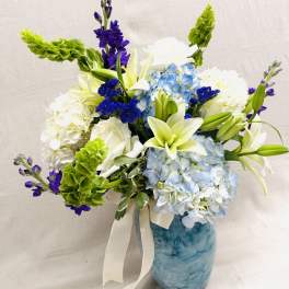 Blue and white floral arrangement in a marbled vase with a ribbon