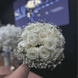 Round bridal bouquet of white roses and baby's breath held in front of a dark background