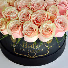 Pink roses arranged in a black round box with gold lettering