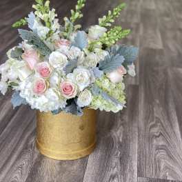 Pink and white roses arranged in a gold round box