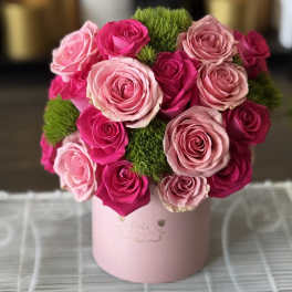 Pink and hot pink roses arranged in a round box with green moss accents