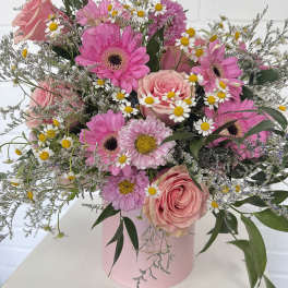 Pink roses and gerbera daisies in a pink hatbox with small white daisies