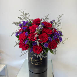 Red roses and purple filler flowers in a black hatbox