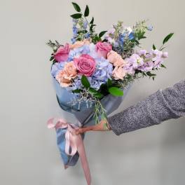 Handheld bouquet of pink roses and pastel blue flowers wrapped in blue paper