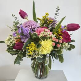 Colorful mixed bouquet with pink roses, yellow carnation, tulips and lavender blooms in a clear glass vase