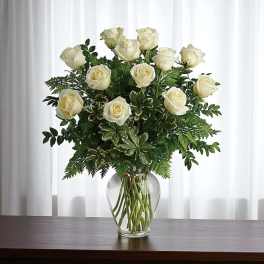 White roses arranged in a clear glass vase with greenery