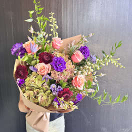 Large bouquet of pink, purple, and green flowers wrapped in brown paper
