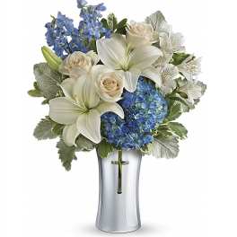 White lilies and roses with blue hydrangea in a silver vase with a cross emblem