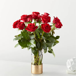 Tall arrangement of red roses in a clear glass vase with a gold base