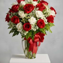 Red and white roses in a clear glass vase with a red ribbon