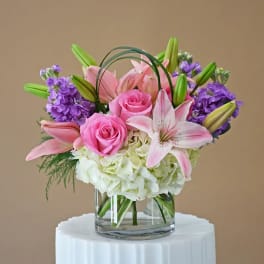 Pink roses and lilies arranged with purple blooms in a glass vase