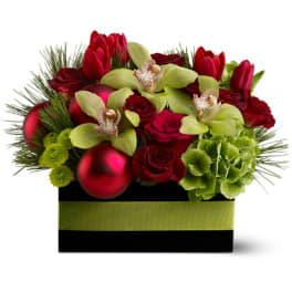 Low red and green holiday arrangement with orchids, roses, tulips and ornaments in a black box.