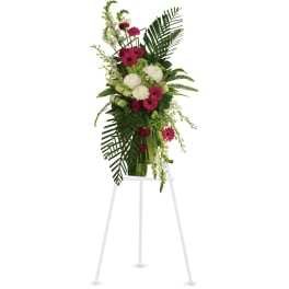 Tall standing spray of hot pink and white flowers in a green vase on a white easel.