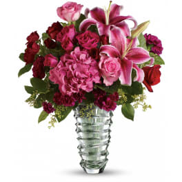 Pink lilies, roses, hydrangea, and red carnations in a tall faceted clear glass vase