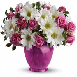 Compact arrangement of white daisies and pink roses in a bright pink glass vase