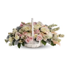Low white basket of soft pink and cream roses with white flowers and ribbon.