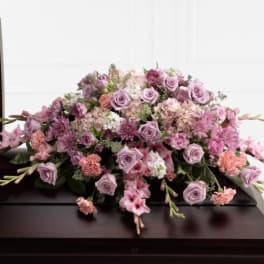 Lavender and pink casket spray of roses and mums on a dark wood casket