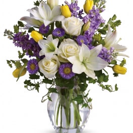 Bouquet of white lilies, white roses, purple flowers, and yellow tulips in a glass vase