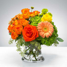 Orange and yellow roses with a peach gerbera daisy in a glass vase