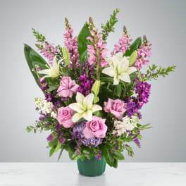 Pink roses and white lilies arranged in a green vase with purple accents.