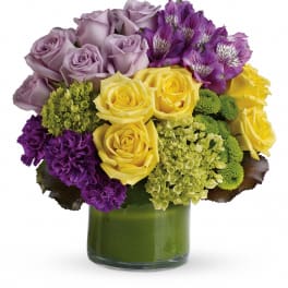 Bouquet of lavender and yellow roses with purple flowers in a green glass vase