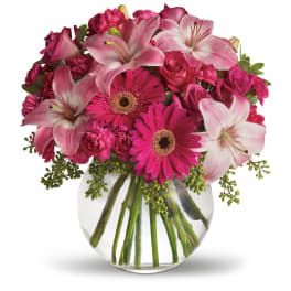 Pink lilies, gerbera daisies, and roses arranged in a clear glass vase