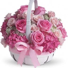 Pink roses and hydrangeas arranged in a white basket with a pink ribbon