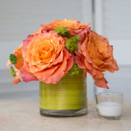 Orange roses arranged in a green glass vase beside a small candle
