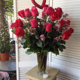 Red roses in a clear glass vase with a heart topper