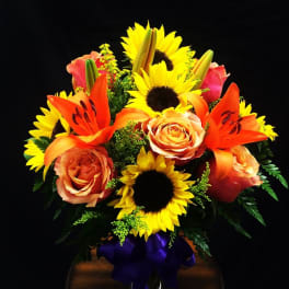 Bouquet of sunflowers, orange lilies, and peach roses with a purple ribbon