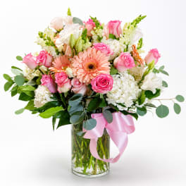 Pink and white mixed flower bouquet in a glass vase with a pink ribbon