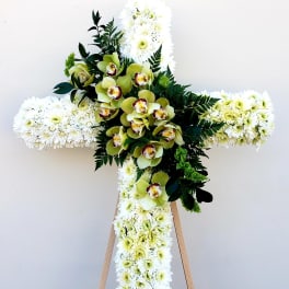 White floral cross with green orchids and dark foliage on an easel