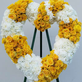 Heart-shaped floral wreath with yellow roses and white blooms on a stand