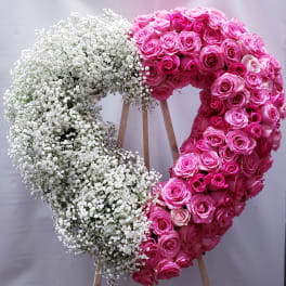 Heart-shaped floral wreath with pink roses and white baby's breath on a stand
