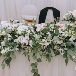 Long white floral centerpiece with greenery on a draped table