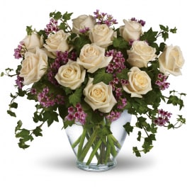 Arrangement of cream roses with small purple flowers and trailing ivy in a clear glass vase