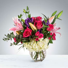 Pink roses and lilies with purple blooms in a clear glass vase