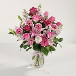 Pink roses and lilies arranged in a clear vase with a polka-dot ribbon.
