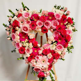 Heart-shaped floral wreath of pink and red roses with gerbera daisies on an easel