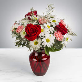 Red roses, white daisies, and pink carnations arranged in a red glass vase