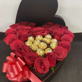 Heart-shaped box of red roses with gold-wrapped chocolates and a red ribbon